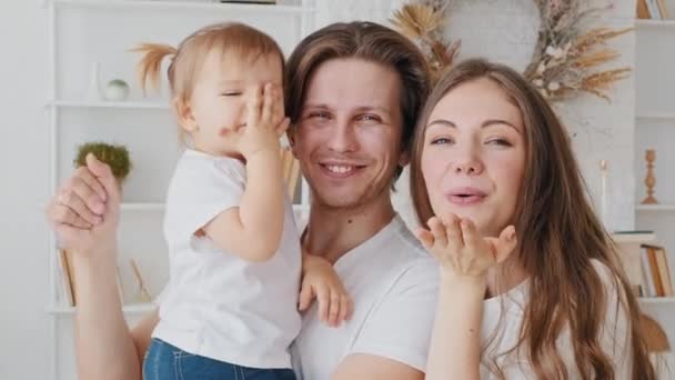 Gelukkig Kaukasische familie jong duizendjarig ouders moeder en vader met kleine dochter pasgeboren sturen lucht kus zwaaien afscheid glimlach, home portret mam, vader met baby kind kijken naar camera — Stockvideo