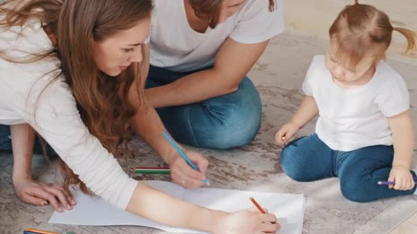 Kaukasische familie trekt samen thuis, jonge zorgzame liefdevolle ouders moeder en vader te helpen kleine dochter peuter kind meisje met tekening te creëren beeld met gekleurde potloden genieten hobby vrije tijd — Stockvideo