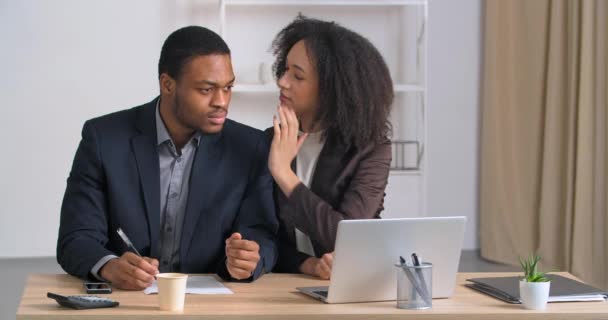 Afro-americano homem de negócios e mulher colegas gerentes sentados à mesa trabalhando menina encaracolado fala segredo no ouvido masculino segredo conta sobre o cara má notícia sente choque chamadas urgentemente usando telefone celular — Vídeo de Stock