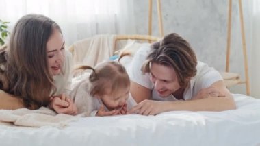 Küçük kızıyla birlikte mutlu bir beyaz anne ve baba evde yatıp gülümsüyor, şefkatli bir anne ve mutlu bir baba çocuk kızıyla kamerayı işaret ederek bağlanıyor.