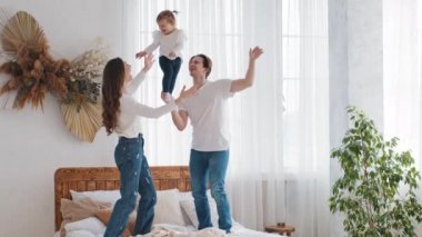 Küçük kızıyla evde oynayan beyaz bir aile, güçlü bir baba, kucağında küçük bir kız çocuğu, bir elinde akrobatik bir poz, annesi çocuğu gülerken yakalar ve çocuğu havaya fırlatır.