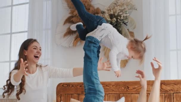 Mutlu küçük kız bebek uçak oyunu oynuyor. Genç baba ve anne ile yatakta eğleniyor. Baba küçük kızı bacaklarıyla kaldırıyor. — Stok video