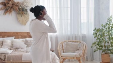 Afrikalı bekar anne hamile afro kadın kulaklıkla müzik dinliyor evde dans ediyor oturma odasında dinleniyor karnını eliyle tutuyor, hamilelik konsepti