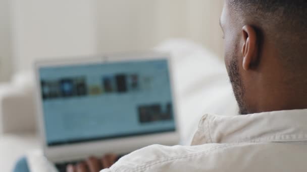 Retour vue homme africain assis à la maison naviguant sur le net à l'aide d'un ordinateur portable. méconnaissable afro noir mixte race guy mâle étudiant à la recherche de film en ligne service recherche musique sur site, écran gros plan — Video