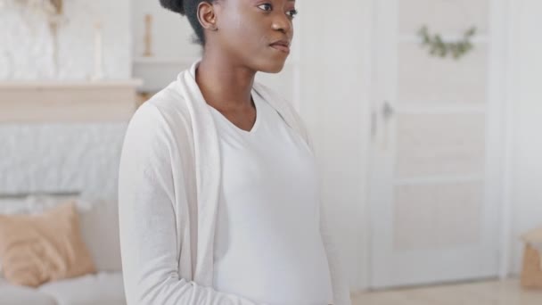 African pregnant woman black future mother stands at home holding belly with hands, caring afro ethnic mixed race man husband brings glass of orange juice, wife drinking enjoy taste, couple hugging — Stock Video
