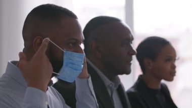 Başarılı iş ortakları farklı yaşlarda Afrikalı meslektaşlar iki erkek müdür ve afro kadın ofiste yapılan toplantıda virüs enfeksiyonundan korunan tıbbi maske takıyorlar.