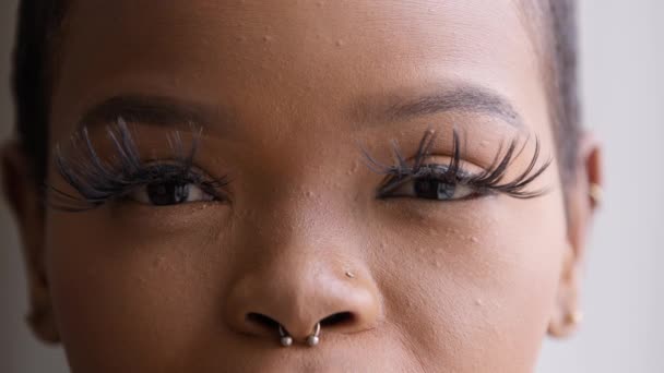 Närbild afrikansk kvinna med långa ögonfransar makeup tittar på kameran nöjd med kosmetisk procedur. Pierced afro flicka klient nöjd med oftalmologi tjänst, framgångsrik laser vision korrigering — Stockvideo