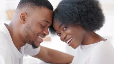 Sevgili Afrikalı çift gülüyor, gülüyor, alınlarına dokunuyor, kameraya bakıyor, romantik milenyum afro erkeği ve mutlu zenci kadın evde sevgi dolu anların tadını çıkarıyor.