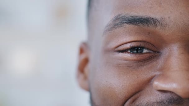 Detailní záběr jednoho černého mužského oka se dívá na kameru šťastným pohledem. Poloviční tvář mladého Afričana. Spokojen afro chlap má dobrý zrak po laserové korekci úspěšný postup používá kontaktní čočky — Stock video