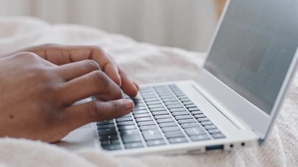 Крупным планом мужские руки с темной африканской кожей, печатающие на клавиатуре современный ноутбук на кровати дома, неузнаваемый афро молодой человек, работающий за компьютером в чате с друзьями, просматривающий сеть, беспроводное соединение — стоковое видео