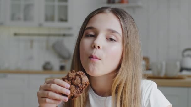 Portrét spokojený šťastný roztomilý hladové dítě holčička dcera školačka jíst lahodné domácí čokoládové sušenky sladké pečivo kousnutí usměvavý pocit potěšení z jídla doma v kuchyni — Stock video