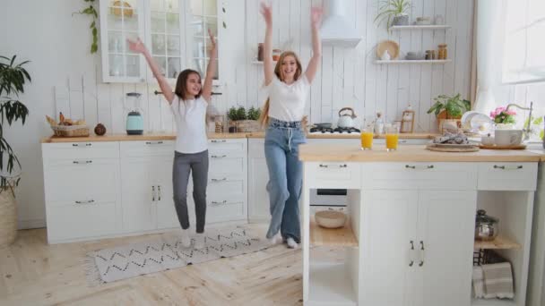 Glad kaukasisk familj vuxen glad ensamstående mor 35s kvinna och skolflicka dotter barn preteen unge dansa tillsammans i köket gör samma handrörelser till musik hoppa dans njuter helg — Stockvideo
