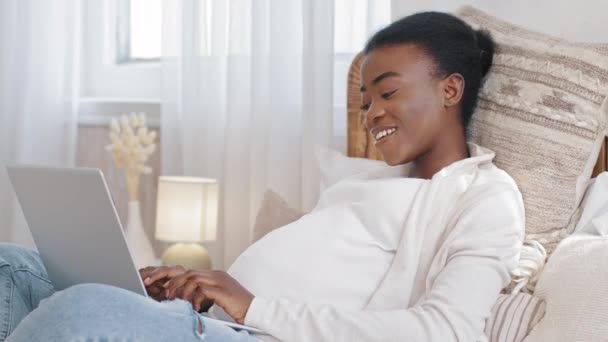 Heureuse fille afro-américaine femme enceinte ethnique noire enceinte mère utilise un ordinateur portable pour communiquer le chat avec des amis qui travaillent à distance en tapant couché dans un lit confortable à la maison, la grossesse et le concept de carrière — Video