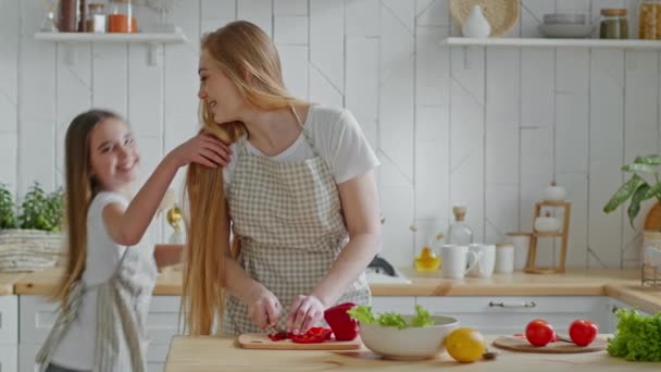 Husmor smuk voksen mor kvinde skærer peber grøntsager kok lækker frisk salat i moderne køkken derhjemme lille teenage pige datter barn løber i værelse hopper hjælper mor, familie tilberedningstid – Stock-video
