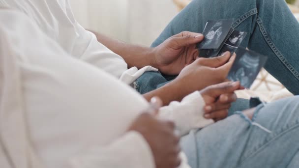 Primo piano coppia africana irriconoscibile futuri genitori in jeans afro americano uomo marito e nero donna incinta guardando ecografie foto immagini godere di nascituro foto, mamma accarezzando pancia — Video Stock