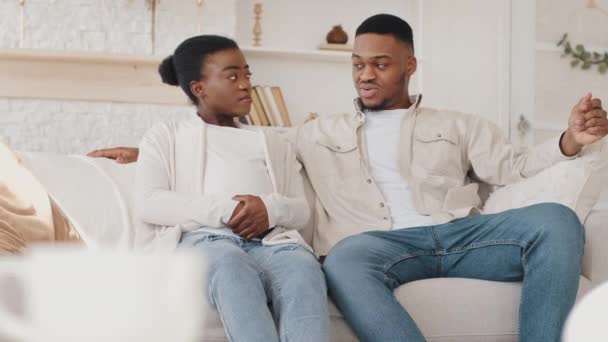 Afro-americano casal sério família futuros pais mulher grávida africana e marido étnico preto sentado em casa sofá sala de estar interior falando discutir plano sobre gravidez do bebê por nascer — Vídeo de Stock
