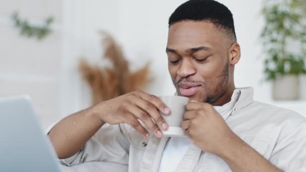 Портрет африканца, пьющего горячий чай из чашки, разговаривающего с камерой и делающего онлайн-звонок из дома. Афро-парень делает видео-чат для дистанционного общения. Выступление мужчины на видеоконференции — стоковое видео