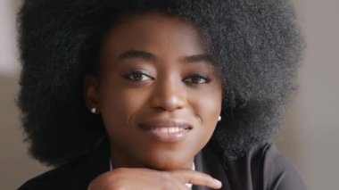 Güzel milenyum kızı kameraya düşünceli bir şekilde bakıyor, cana yakın gülümsüyor. Kibar şirket çalışanı kurumsal görgü kurallarına uyar. Çekici Afrikalı Amerikalı siyahi iş kadını