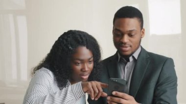 Çok ırklı genç çift, birlikte cep telefonuna bakarak sosyal medya başvurularını kontrol etmeyi, video alışverişini ve elektronik ticaret uygulamasını başarıyor. Modern teknolojiyle ofiste ara vermek..