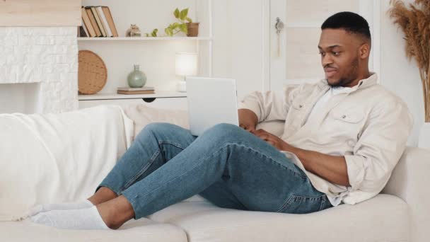 Sebevědomý zaměřený africký úspěšný freelance obchod muž zahraniční mezinárodní afro student sedí na gauči s notebookem používá počítačové aplikace web on-line služby v síti pracovní studie vzdáleně od domova — Stock video