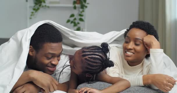 Portrait of afro american ethnic black mixed race family lying covered with white blanket waving at camera hello smiling, little african girl daughter forbids mom and dad to greet stops hand gestures — Stock Video