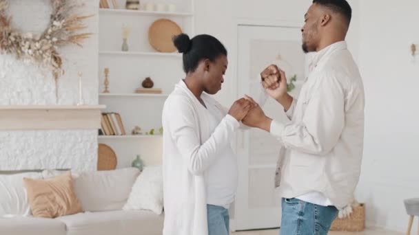 Glada afrikanska unga föräldrar afro gift par familj gravid kvinna fru och svart man man man dansar hemma njuta av graviditeten aktivt flytta dans till musik hålla händerna glädja ofödda barn — Stockvideo