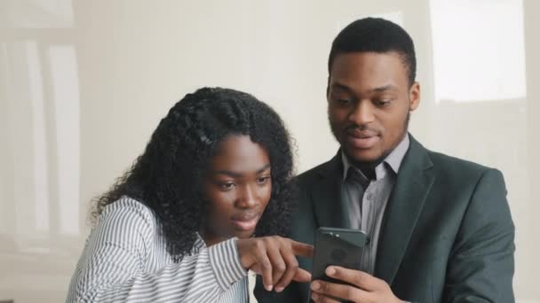 Compañeros multiétnicos pareja joven lograr día de trabajo comprobar aplicación de redes sociales ver vídeo de compras en la aplicación de comercio electrónico mirando el teléfono celular juntos. Ruptura en el trabajo en la oficina utilizando tecnología moderna. — Vídeo de stock