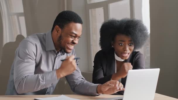 Jóvenes trabajadores de oficina afroamericanos, chico y chica, trabajan con éxito junto con la computadora portátil de concentración en la oficina. Feliz mujer de negocios satisfecha y el hombre recibe buenas noticias carta, regocijarse — Vídeo de stock