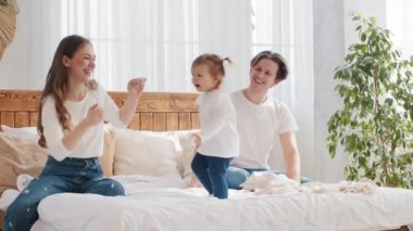 Aile sabah yatak odasında eğleniyor, küçük kız çocuk yatakta müzik eşliğinde dans ediyor baba ve anne desteği seviniyor kız dansçı çocuk puanları kameraya el sallıyor anne merhaba diyor.