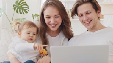 Küçük kızıyla birlikte küçük bir kanepede oturan beyaz bir ailenin portresi. Bilgisayar başında küçük bir kızın işaret parmağını göstererek elma yerken görüntülü konuşma yapmak için bilgisayarı kullanıyor.