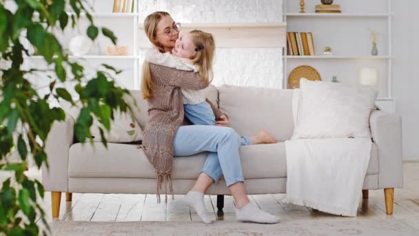 Mengasuh ibu yang penyayang pengasuh wanita dewasa peluk peluk peluk putri kecil yang lucu duduk di sofa mengungkapkan cinta, anak kecil tertawa menikmati berpelukan dengan ibu di rumah — Stok Video