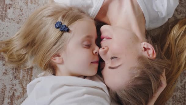 Top view single mother adult caucasian woman lies on home floor with little beloved daughter adorable child kisses girl on forehead touches noses talking laughing, tenderness love, shooting from above — Stock Video