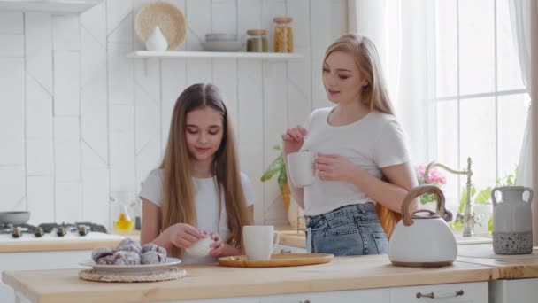 少女女学生的女儿和妈妈一起站在厨房里，把糖倒进杯子里喝茶。白种人家庭成年母亲和女儿在早上的谈话中喝咖啡卡布奇诺 — 图库视频影像