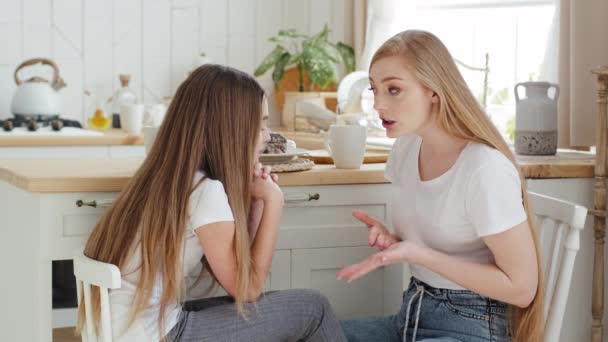 Ciddi anne, sarışın, uzun saçlı beyaz kadın modern mutfakta kızıyla birlikte sandalyede oturuyor. Genç kız, tecrübelerini paylaşıyor. Haberler ev içi iletişim konuşmalarında olanları açıklıyor. — Stok video