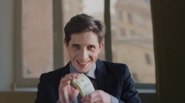Kafkasyalı mutlu iş adamı lideri portresi, zafer kazanmanın sevincini yaşıyor. Yatırım kredisi, para dolu banknotların arkasına saklanıyor. Ofiste poz veren kameraya bakıyor.