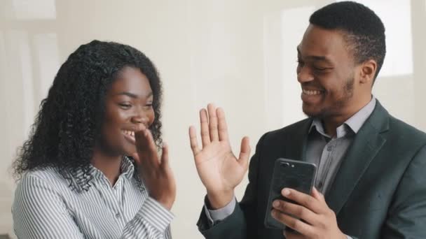 Glad säker smarta unga multietniska kollegor tittar på mobiltelefon kontrollera sociala medier ansökan få smsmed goda nyheter tillsammans ge high five. Pausa på jobbet med modern teknik. — Stockvideo