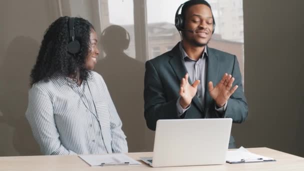 Emocionados estudiantes de negocios de raza mixta feliz hombre de negocios usan auriculares que se divierten escuchar música. Hombre africano sonriente con traje bailando al ritmo en la oficina del trabajo. Concepto de educación a distancia — Vídeos de Stock