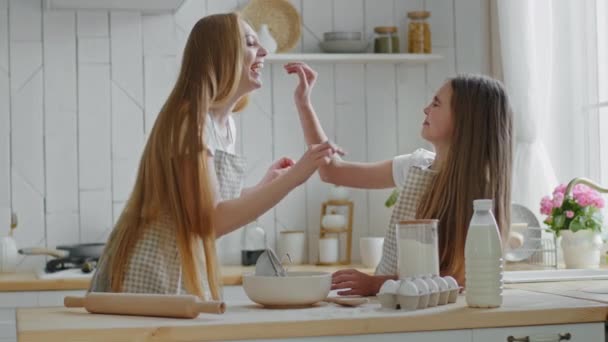 Glad kaukasisk familj glad mor med långt hår och aktiv tonåring flicka dotter barn matlagning tillsammans i hemmet kök lek spel att ha roligt smeta näsan till varandra med mjöl skrattar — Stockvideo