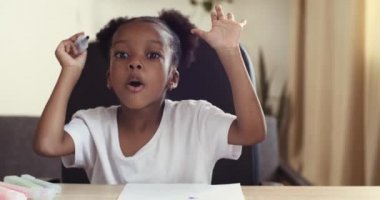 Web kamerası görüntüsü küçük Afro-Amerikan çocuk tatlı kız konuşuyor parlak kalemlerle resim çiziyor renkli kalemlerle yorum yapıyor yaratıcı süreç üzerine video çekiyor blog için, ev eğlencesi konsepti için.