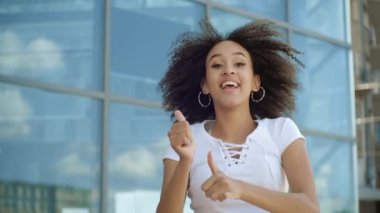 Etkin Afro-Amerikan etnik kadın atlıyor, dans ediyor, baş parmaklarını kaldırıyor, zaferi açık havada müzikle kutluyor. Neşeli kıvırcık kız, kalp atışını yavaş çekimde gösterir.
