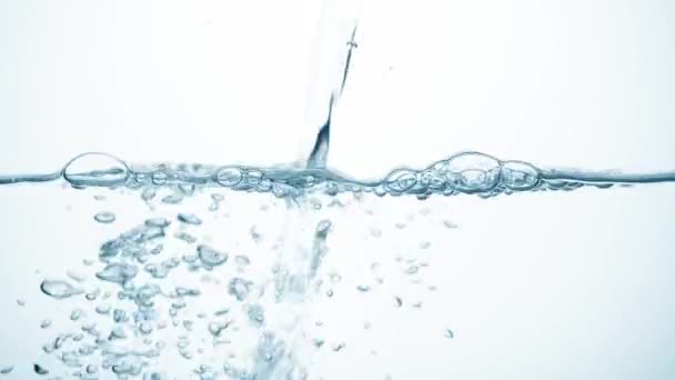 Freshness of a clear blue liquid on white background. Brilliant stream of water in slow motion falls on smooth clean surface, creating air bubbles, drop splashes and ripples after falling, side view — Stock Video