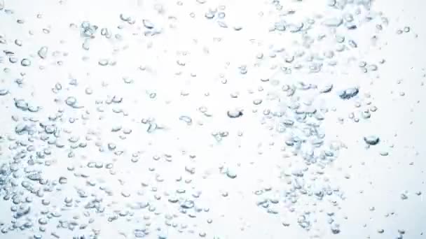 Le flux d'eau au ralenti tombe sur une surface lisse et propre, créant des bulles d'air, laissant tomber des éclaboussures après la chute. Fraicheur d'un liquide bleu clair versé dans un récipient transparent sur fond blanc — Video