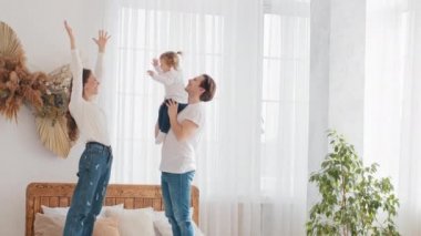 Anne-baba, genç, evli, beyaz, aile babası, kucağında küçük bir kız çocuğu, havaya kaldırıyor, el kaldırıyor, çocuk tekrar ediyor, anne ve baba gülümsüyor, mutlu hafta sonları, yatak odasında, yatak odasında, mutlu hafta sonları.