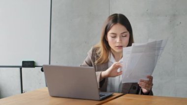 Kafkasyalı genç iş kadını yönetici kadın öğrenci uzman kız şık bir ceket giyiyor ofiste oturuyor evrakları tutuyor bilgisayardaki verileri kontrol ediyor bilgisayardaki bilgisayarları kullanıyor evrak işlerini yapıyor