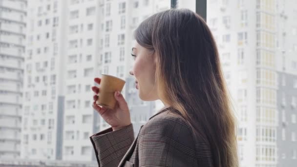 Caucásico joven millennial mujer de negocios líder jefe especialista en puestos profesionales en la oficina mirando por la ventana en rascacielos ciudad bebidas té café de cartón taza vueltas cabeza mira a la cámara — Vídeos de Stock