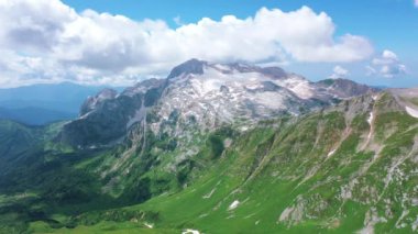 Beyaz bulutların altında kar taşları ve çimlerle kaplı Kafkasya 'nın görkemli doğasının Oshten tepesinden Mountain Fisht' e kadar uzanan hava manzarası. Güneş yazın ışıldıyor, Adygea, Rusya