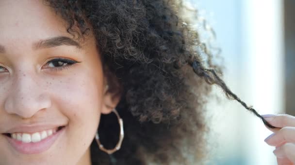 Hermosa joven africana confiada se ríe. Estudiante étnico americano feliz, peinado afro rizado, pendientes perforados redondos, maquillaje ligero y sonrisas pecas y muestra sus dientes blancos saludables — Vídeos de Stock