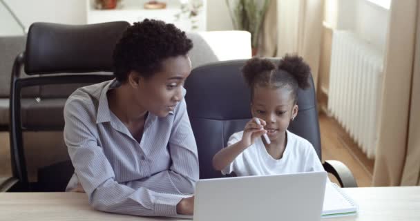 Mãe africana ensina pequena filha pré-escolar bonito em casa sentado à mesa mostra informações sobre laptop lição on-line explica a informação do conhecimento da criança ajuda com lição de casa, conceito de educação — Vídeo de Stock