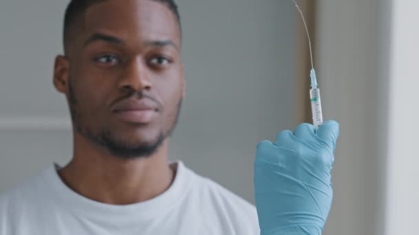 Close-up female hand in blue glove holds syringe with vaccine presses sprinkles with medicine portrait of african american man patient refuses vaccination says no puts palm in front of him disagreeing — Stock Video
