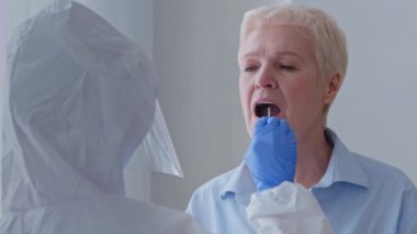 Portrait unrecognizable lab technician female doctor in protective suit takes swab from grandma patient old caucasian woman elderly lady for coronavirus covid-19 virus at home, medicine nurse indoors